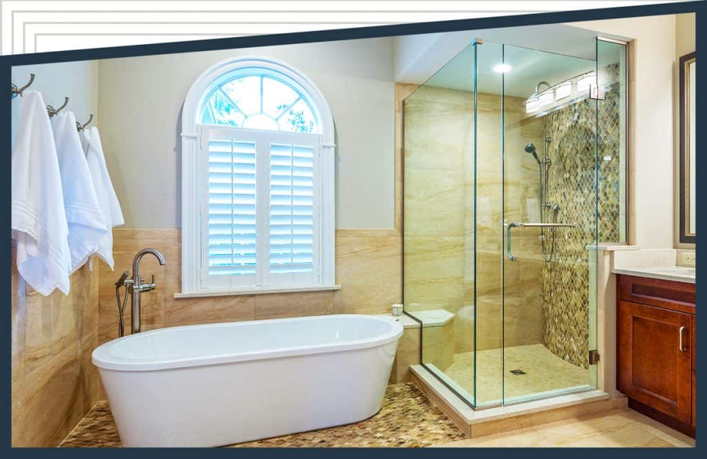 A bathtub underneath a window with towels hanging nearby. An Aldora glass corner shower with Peterson Shower Doors is next to the sink and vanity.