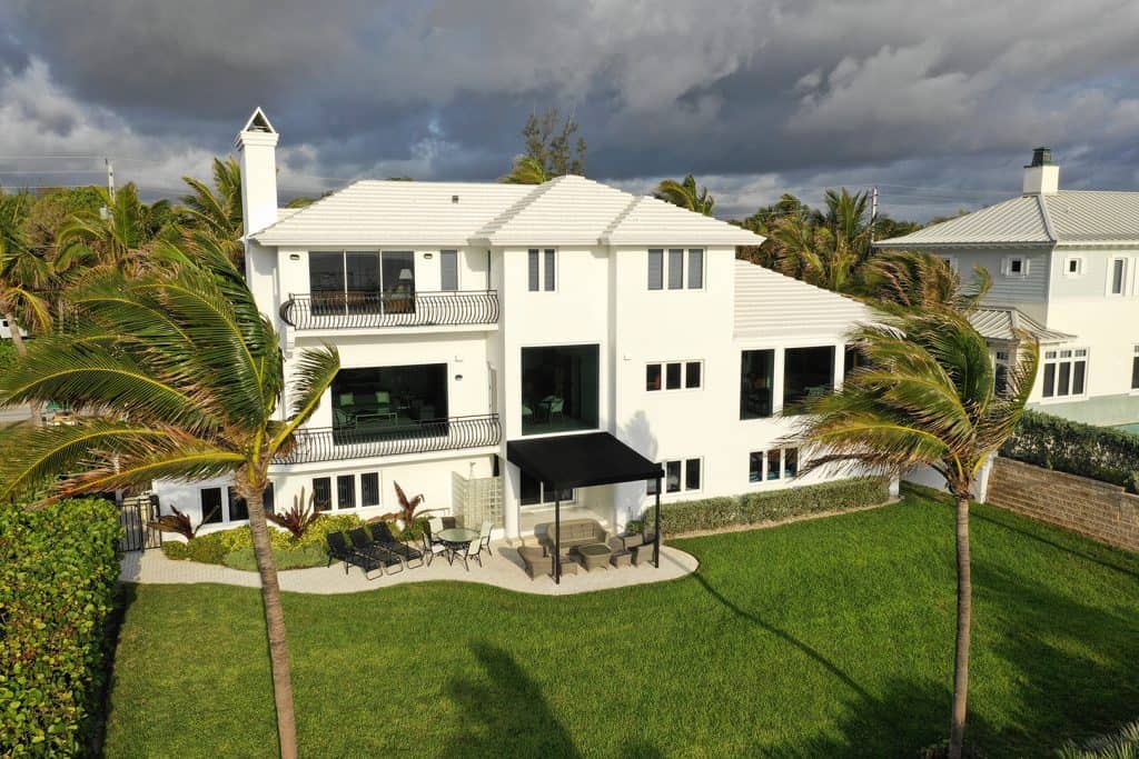 Drone view of large white home with black trim, front view, residential neighborhood, multiple double panel impact windows, FS-300 Maxi View Impact Storefront windows by Aldora, manicured lawn, palm trees, tropical environment