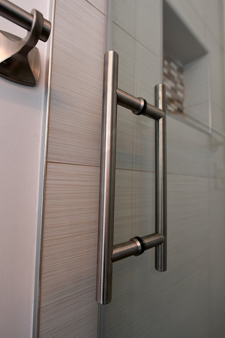 Close up view of chrome door handle attached to glass shower door by Aldora, slate grey tile in background