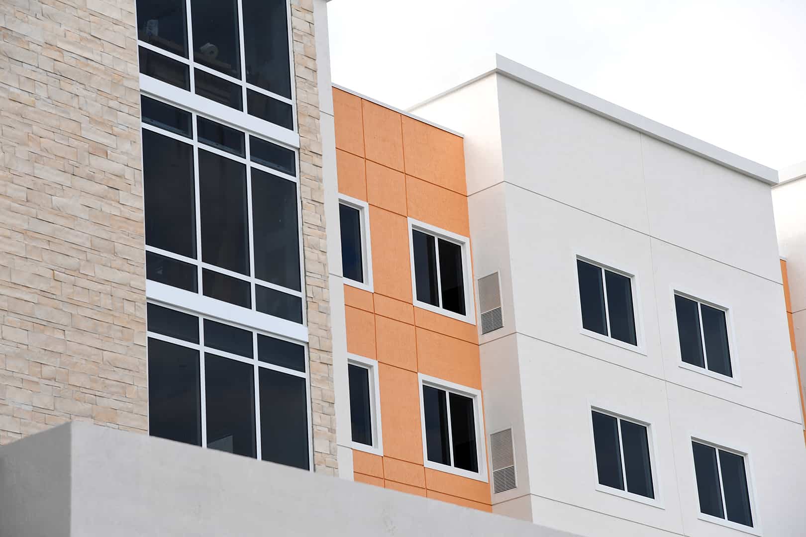 Angled zoomed in view of multi-level orange and grey building with stone accents, grid of FS-300 Impact Front Set windows and double-paned windows with aluminum framing by Aldora