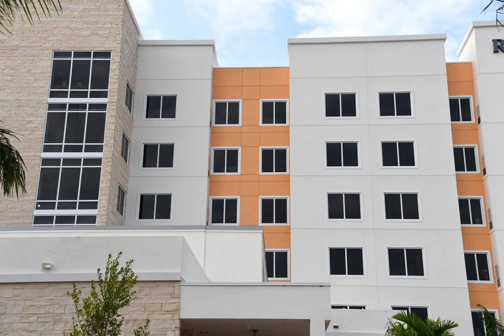Multi-level orange building with grey outsets and stone accents, FS-300 Impact front set double panel   windows with aluminum framing by Aldora, grid curtain wall windows in stone accent section of building