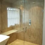 Glass wall walk-in shower by Aldora, beige ceramic tile, shower seat, chrome finish, soaker tub to left of image