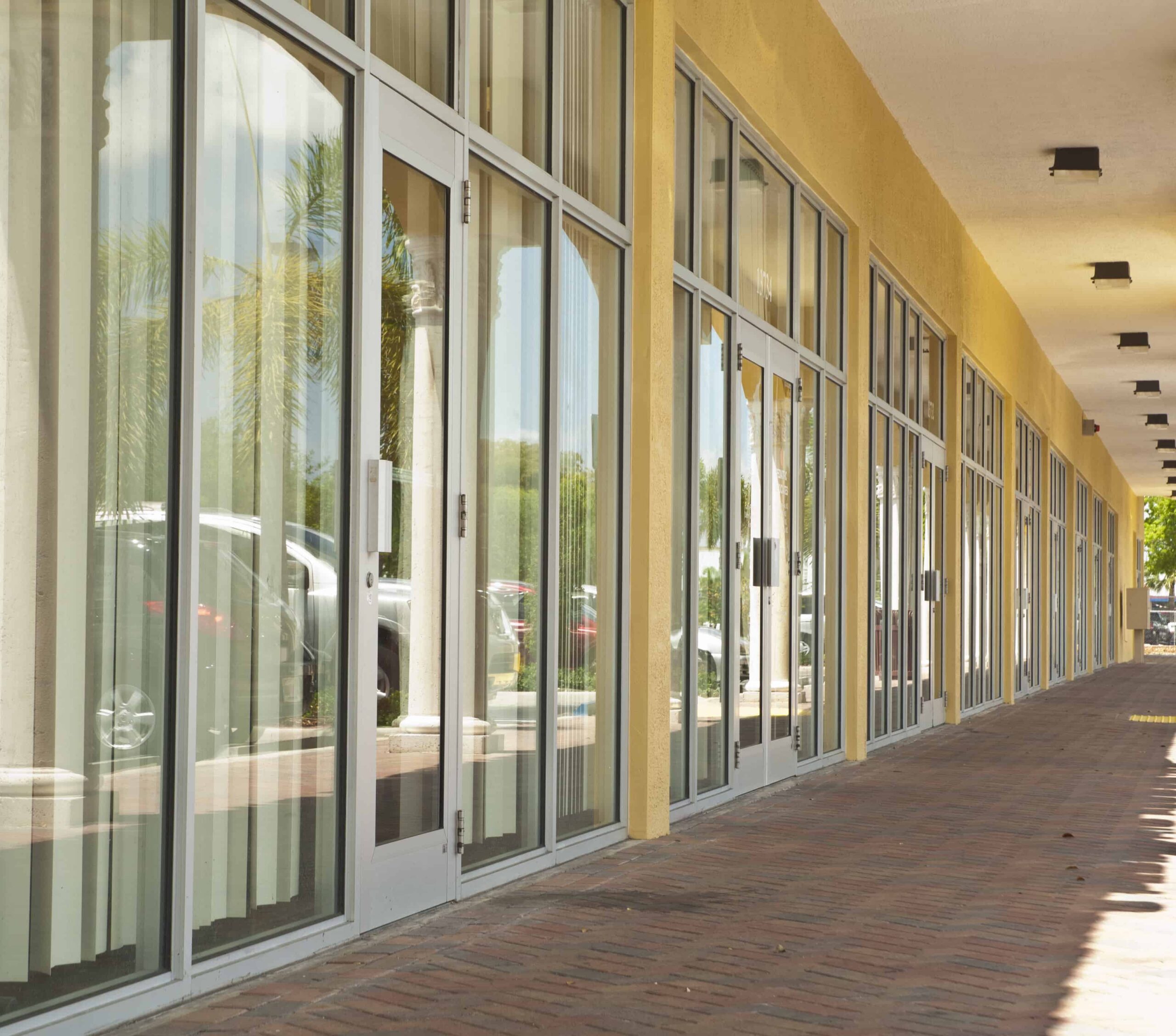 Windows and Aldora non-impact glass doors line the wall of orange building. Brick paved patio with covering runs in front of the doors.