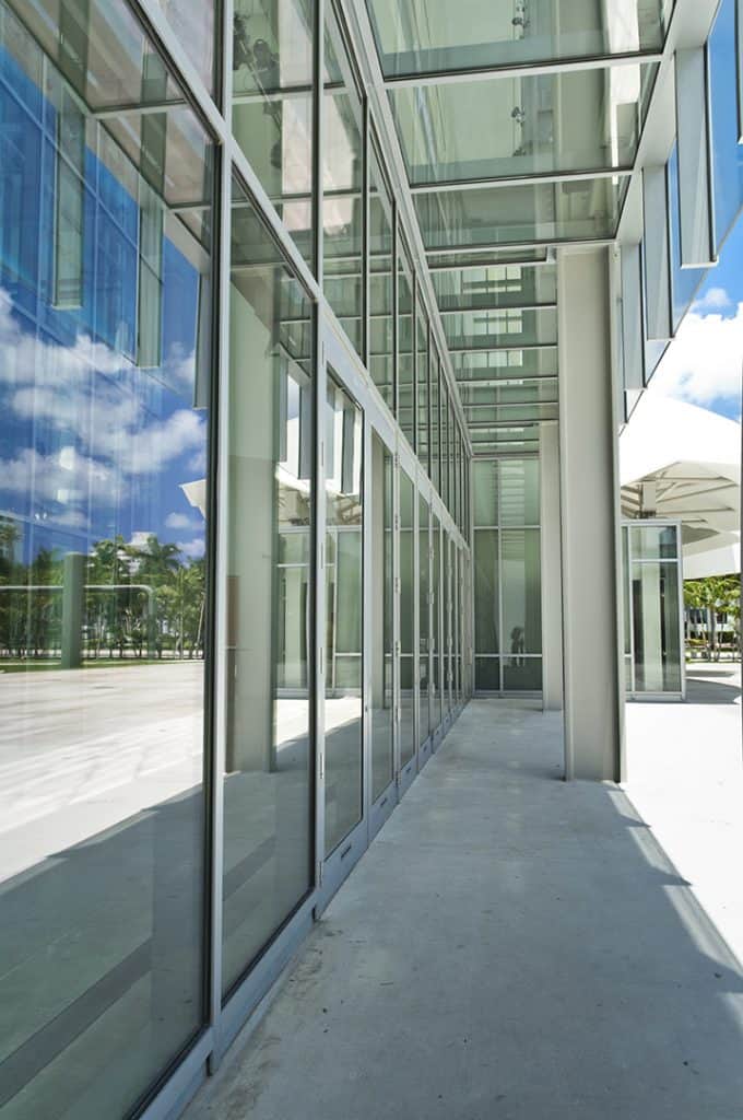 Side angle view of K2-Summit Impact Doors by Aldora, doors are surrounded by glass impact curtain walls, sidewalk leading to doors