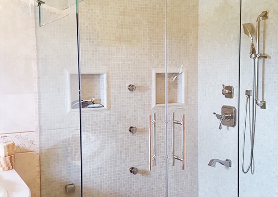 A glass enclosed shower features Aldora towel bars and handles, tiled walls, and faucets 