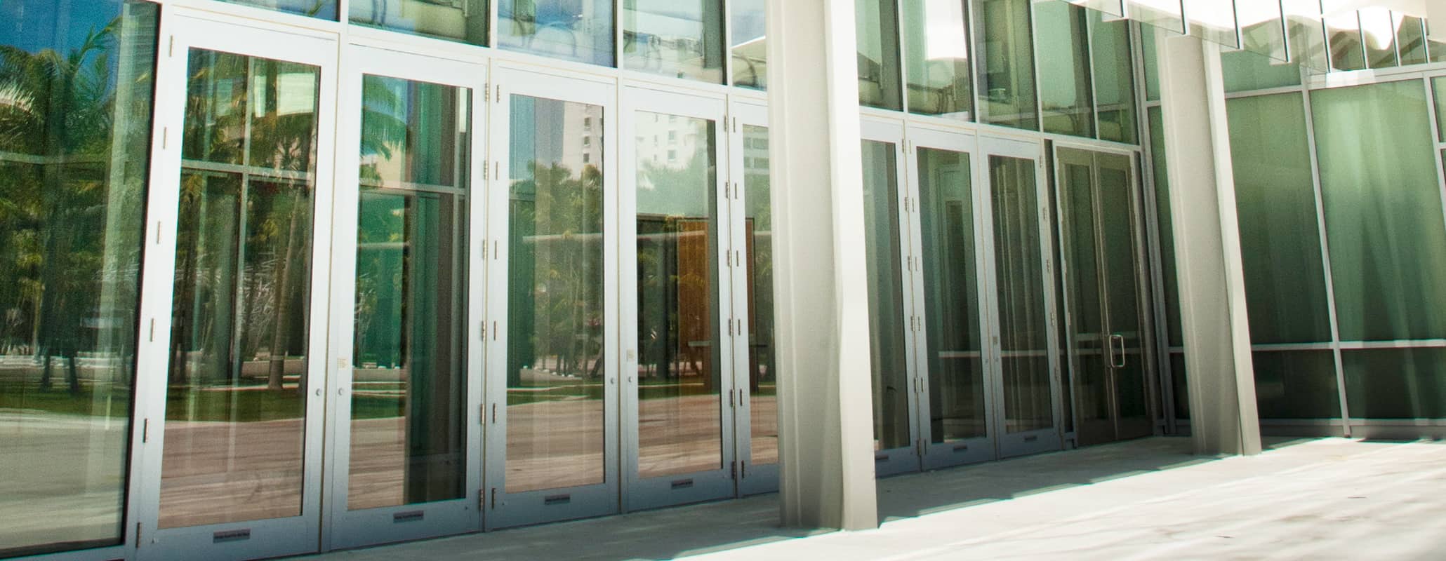 Angled view of commercial glass doors by Aldora, curtain wall windows above and surrounding doors to create building walls, side walk in front of building