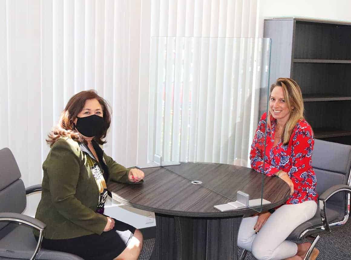 2 Women siting at a table with a glass partition in the middle of the table.