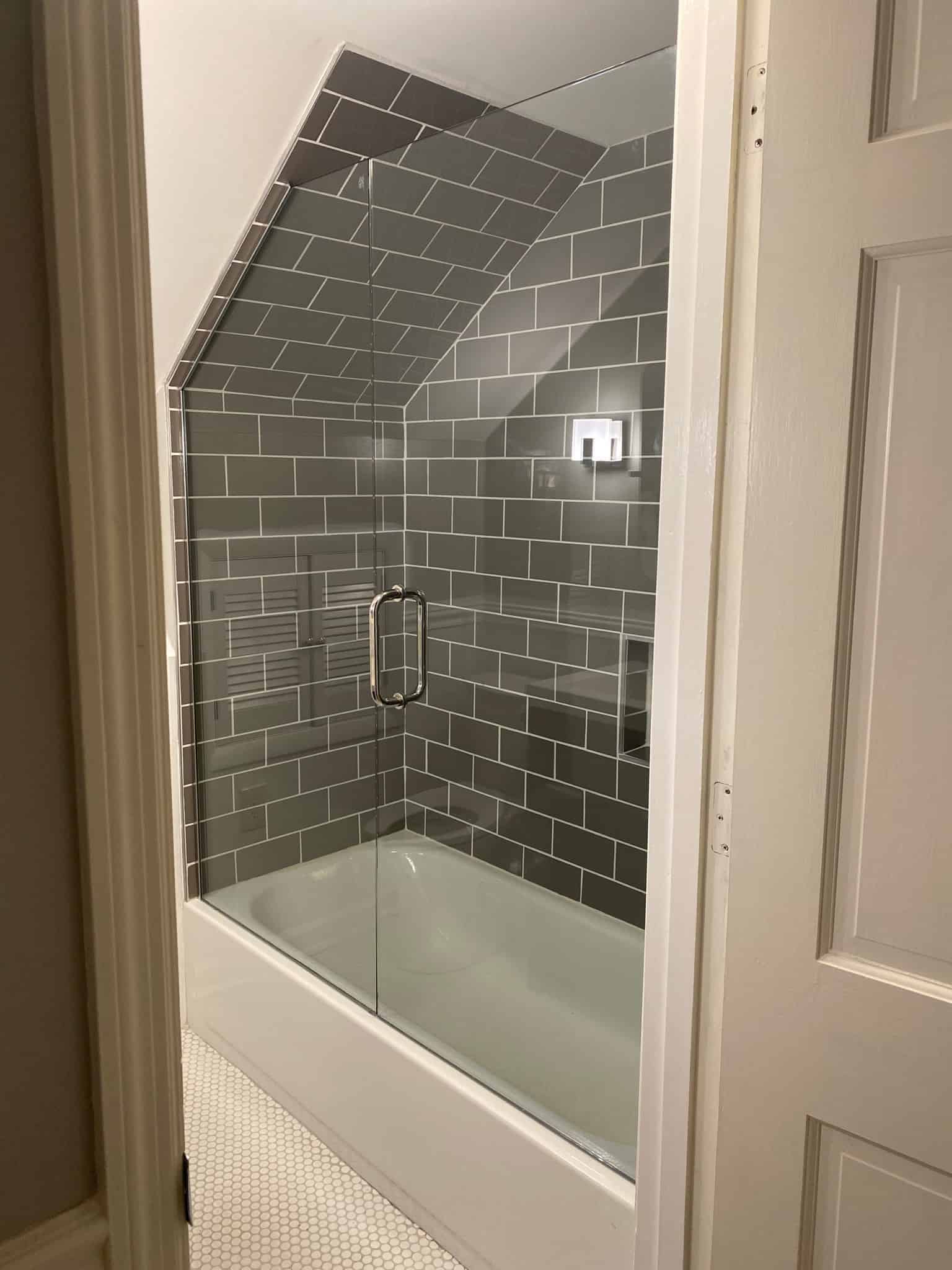 Custom shower door with pull handle in grey tiled bathroom from Aldora